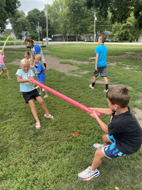 a boy and girl play tug-of-war with a pool noodle